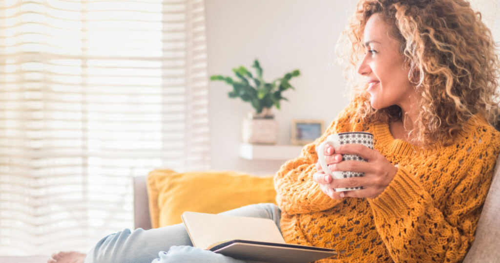 Woman have relax at home with cup of tea and book - reading activity for adult beautiful female people - enjoying quiet lifestyle indoor and long blonde curly hair - happy adult female indoor - people