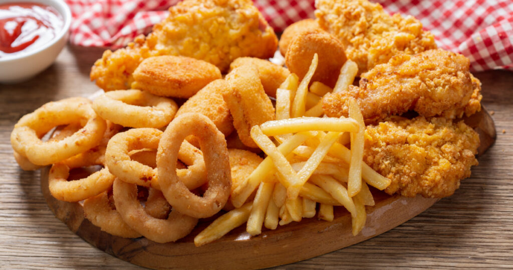 fast food meals : onion rings, french fries, chicken nuggets and fried chicken on a wooden table