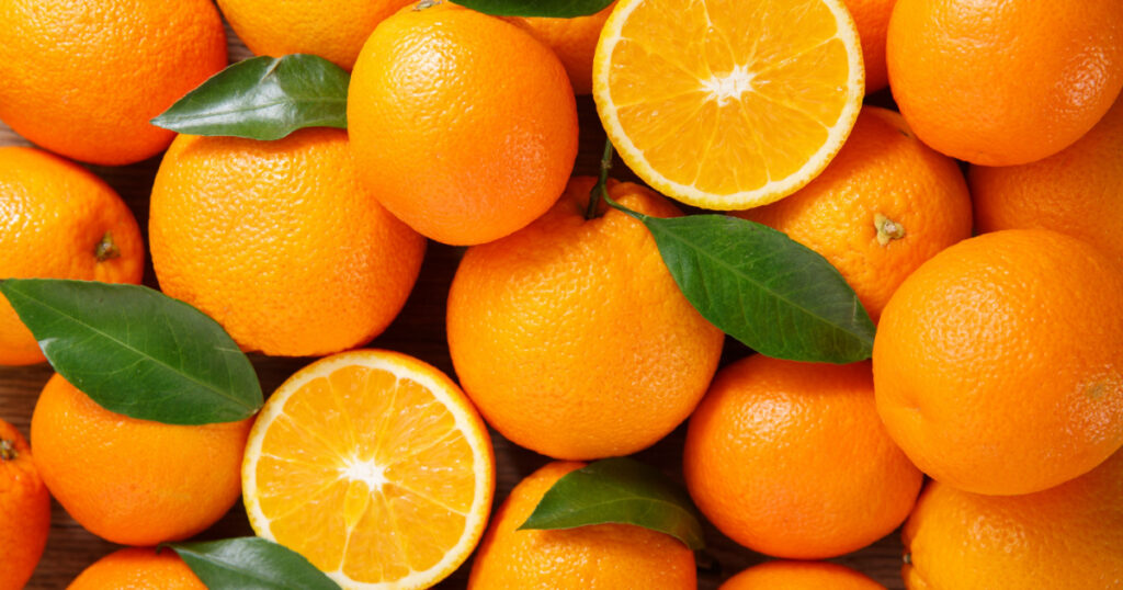 fresh orange fruits with leaves as background, top view