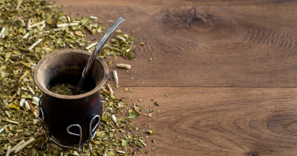 Traditional mate made of calabash over a wooden table with yerba mate scattered over it.
