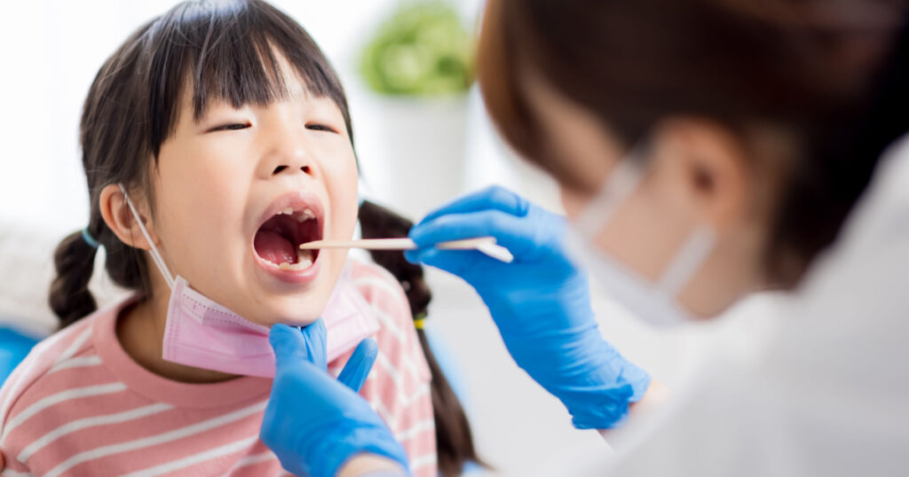 female pediatrician doctor examining throat of a little ill girl