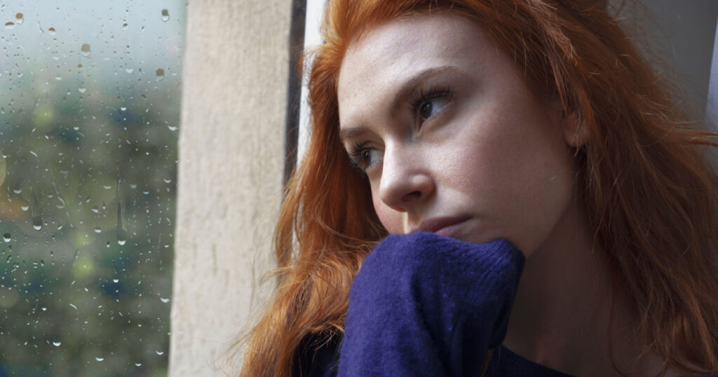 Portrait of worried girl looking through the window at home
