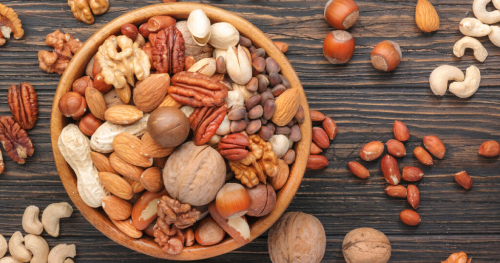 Assortment of nuts in bowls. Cashews, hazelnuts, walnuts, pistachios, pecans, pine nuts, peanuts, macadamia, almonds, brazil nuts. Food mix on wooden background, top view, copy space