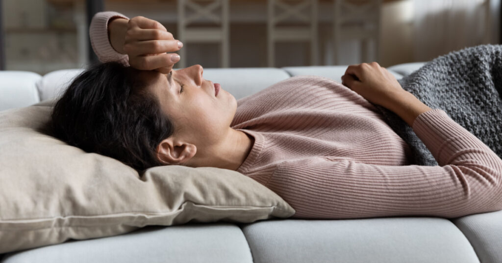 Weak sick millennial hispanic female lying on couch at living room feel dizzy migraine headache suffer from sleep problem disorder. Young latin lady wake up after nap lie on back raise arm to forehead
