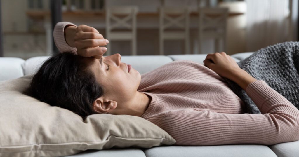 Weak sick millennial hispanic female lying on couch at living room feel dizzy migraine headache suffer from sleep problem disorder. Young latin lady wake up after nap lie on back raise arm to forehead