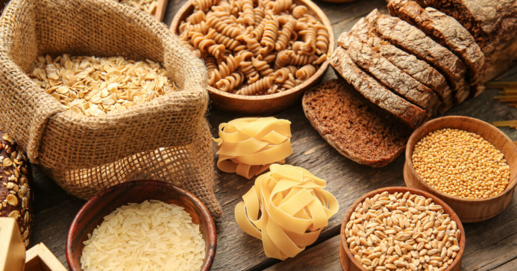 Different cereals, raw pasta and bread on wooden background, closeup