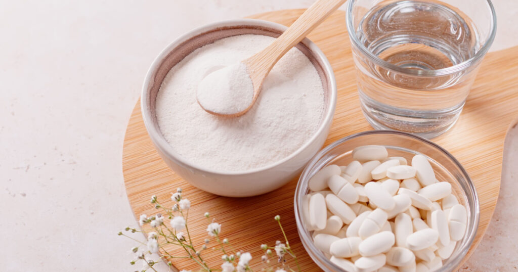 Collagen powder, pills and glass of water on wooden tray, top view