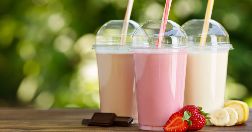 set of different milkshakes in disposable plastic glasses on wooden table outdoors