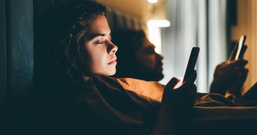 Couple with smartphones in their bed. Mobile phone addiction. Bored distant couple ignoring each other lying in bed at night while using mobile phones.