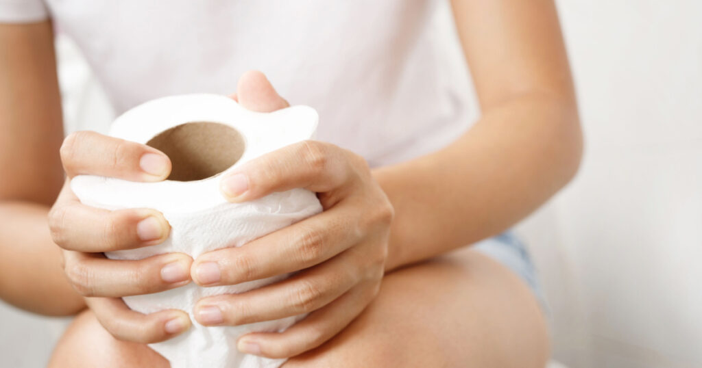 portrait of a woman suffers from diarrhea his stomach painful. ache and problem. hand hold tissue paper roll in front of toilet bowl. constipation in bathroom. Hygiene, health care concept.