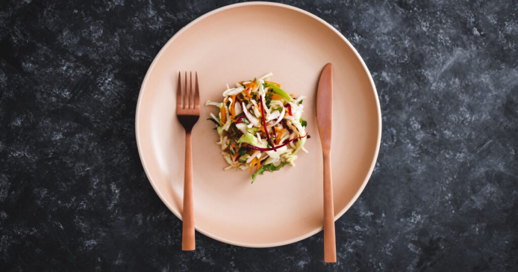 big plate with small amount of salad in the centre, concept of dieting and calorie restrictions