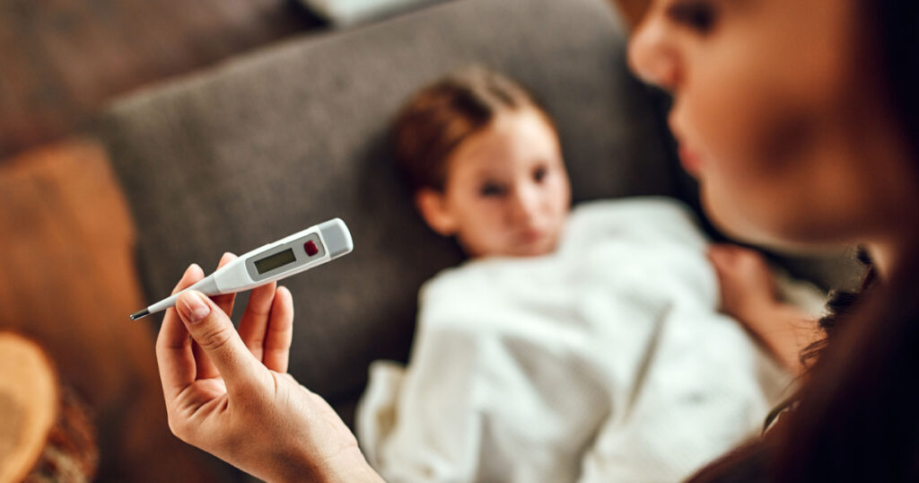 The child has a high fever. Mom looks at the thermometer, measures her daughter's temperature.