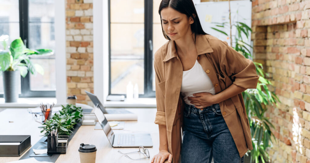 Bad period. Full length view of the caucasian woman suffering with menstrual stomach ache or feeling hurting stomach in her office