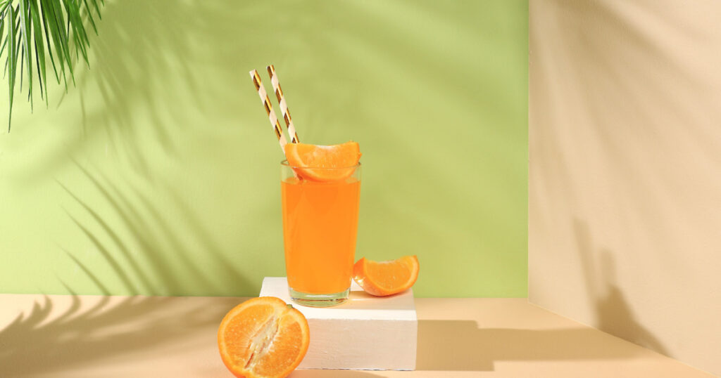 Modern still life with citrus fruits, orange juice and oranges on a pastel background with long hard shadows, minimal detox diet concept, summer vitamin drinks, selective focus,