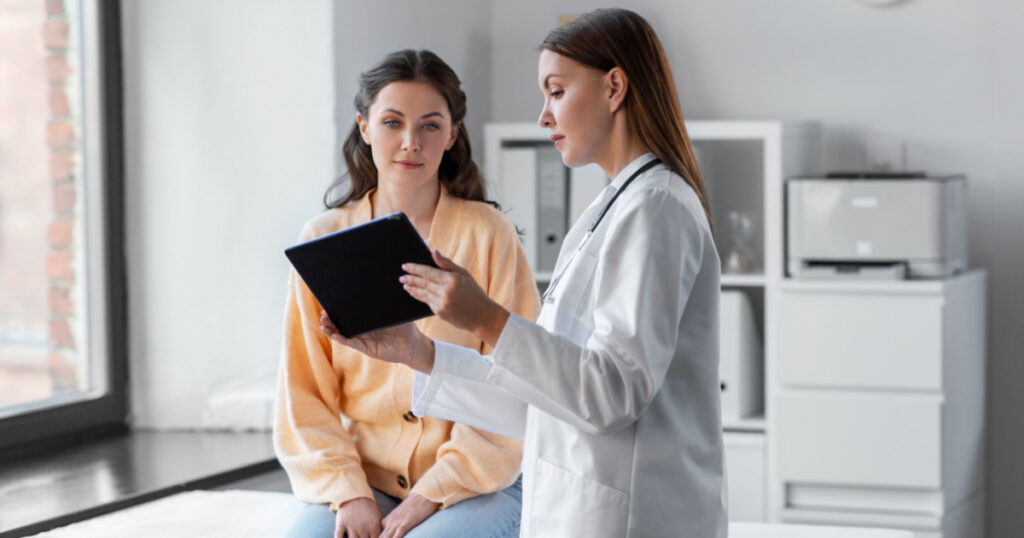 medicine, healthcare and people concept - female doctor with tablet pc computer talking to woman patient at hospital