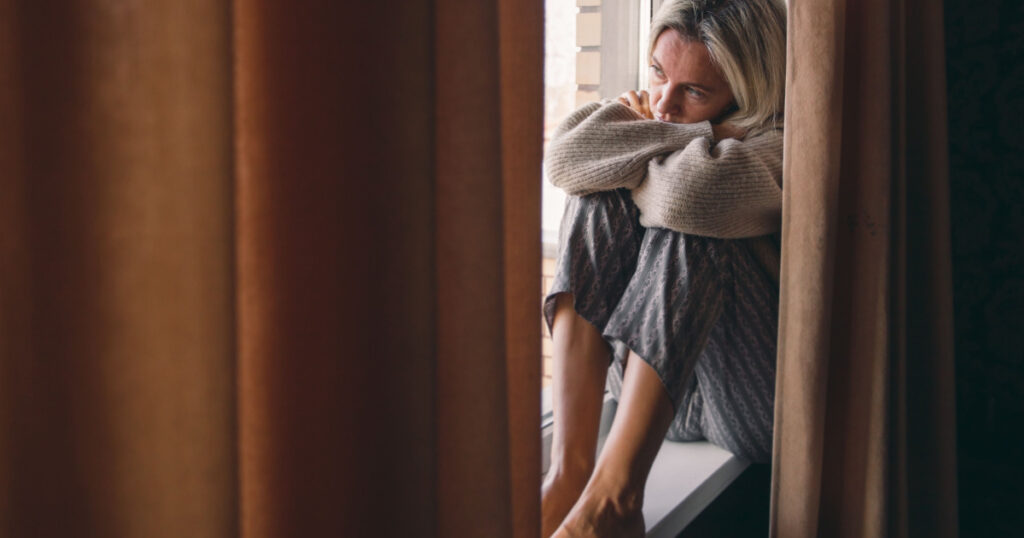 Adult upset woman is sitting by the window. Alone middle aged female in depression is experiencing severe stress
