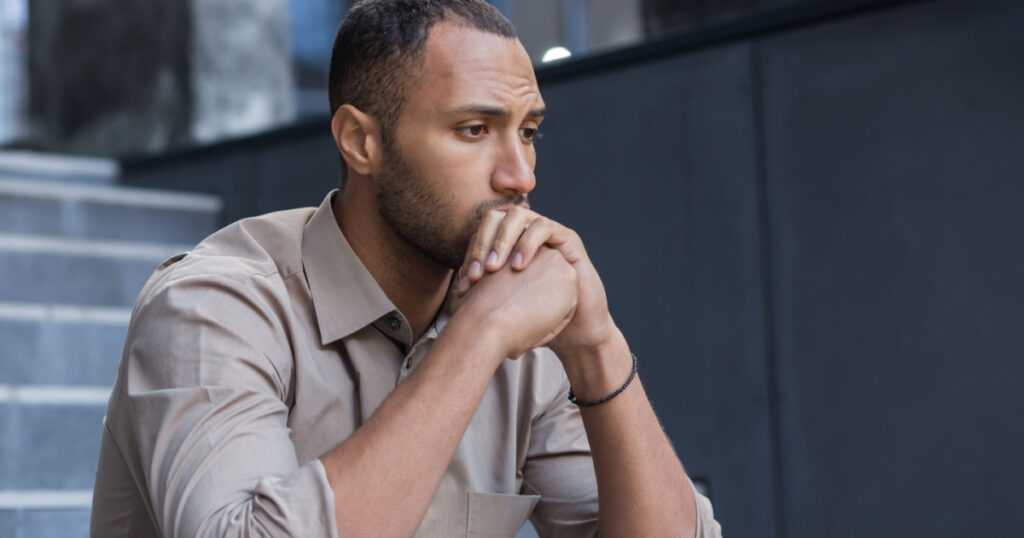 Portrait of a serious and sad hispanic.african american man. He sits sullenly outside on the stairs, holds his head in his hands, looks to the side.
