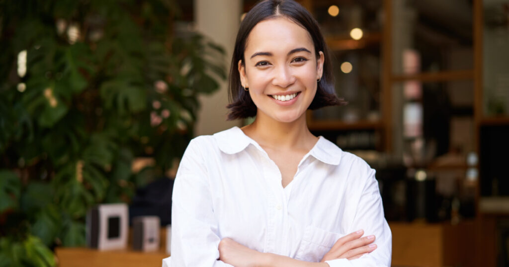 Portrait of smiling asian girl in white collar shirt, working in cafe, managing restaurant, looking confident and stylish.