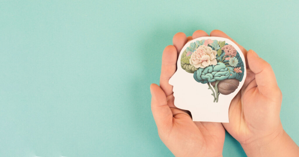 Hands holding paper head, human brain with flowers, self care and mental health concept, positive thinking