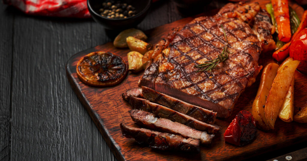 Grilled beef steak on the dark wooden background.