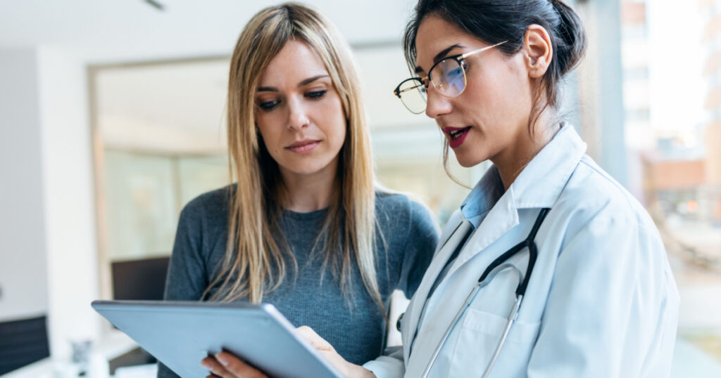 Shot of beautiful female doctor talking while explaining medical treatment with digital tablet to patient in the consultation.