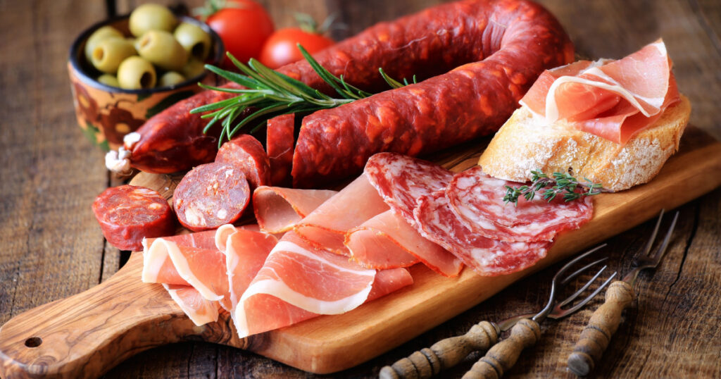 Cured meat platter of traditional Spanish tapas - chorizo, salsichon, jamon serrano, lomo - erved on wooden board with olives and bread
