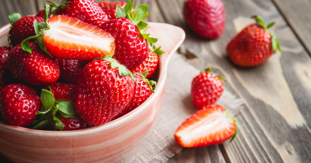 Fresh strawberries in a bowl on wooden table with low key scene.
