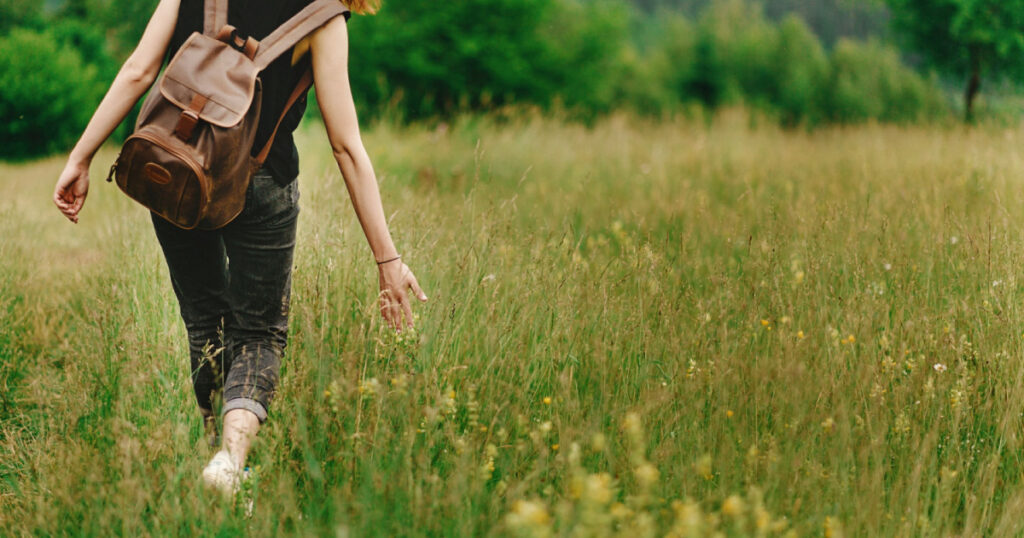 stylish hipster woman walking in grass and holding in hand herb wildflowers in summer mountains, travel concept, peaceful relaxing moment. happy earth day