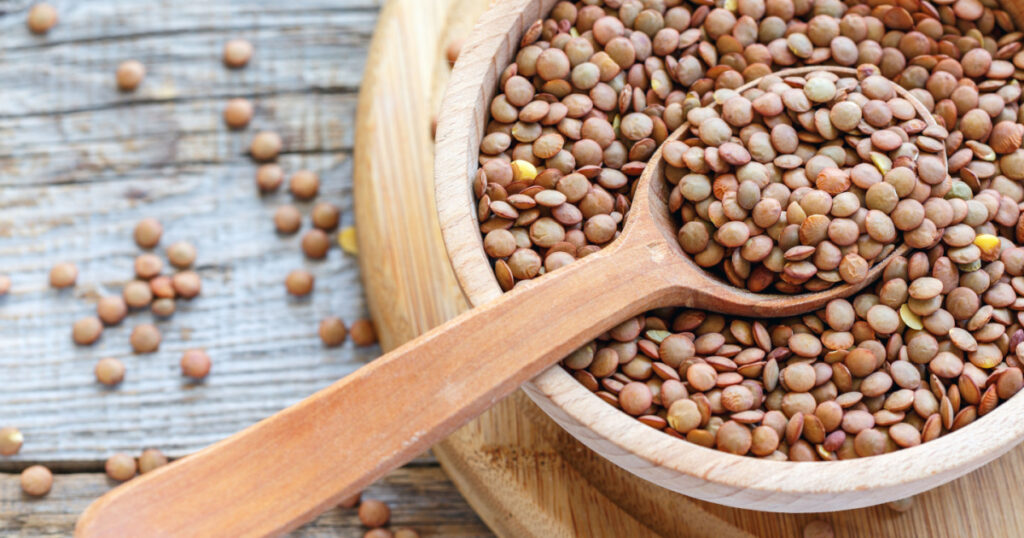Lentils and spoon in a wooden bowl close up on an old table.