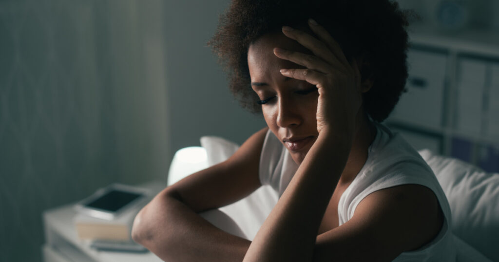 Sad depressed woman suffering from insomnia, she is sitting in bed and touching her forehead, sleep disorder and stress concept
