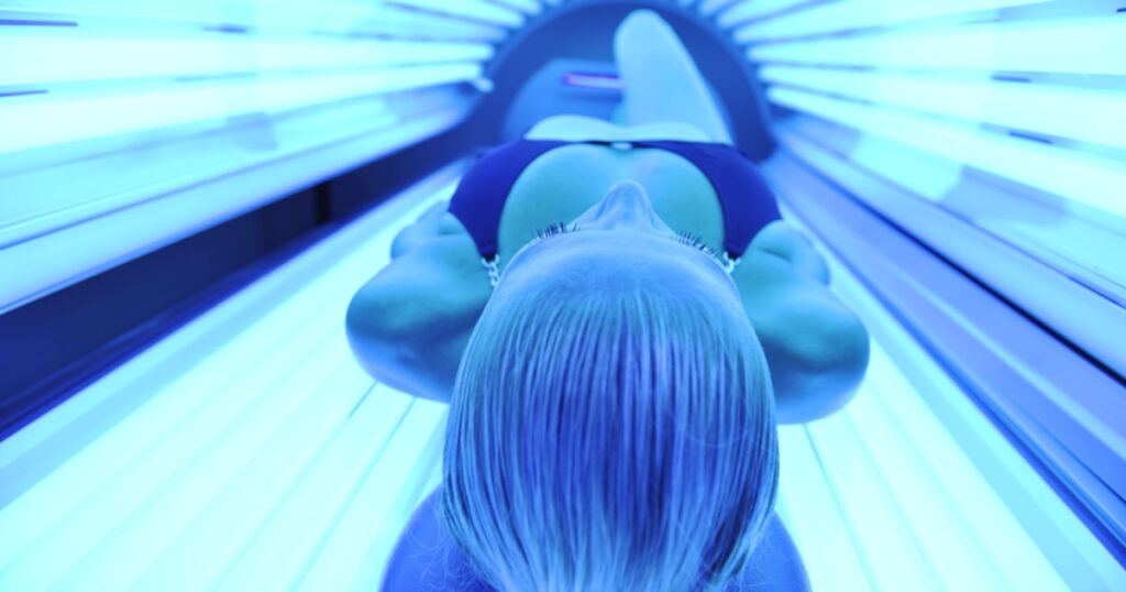 young woman at laying on solarium bed and get brown skin tone ready for summer