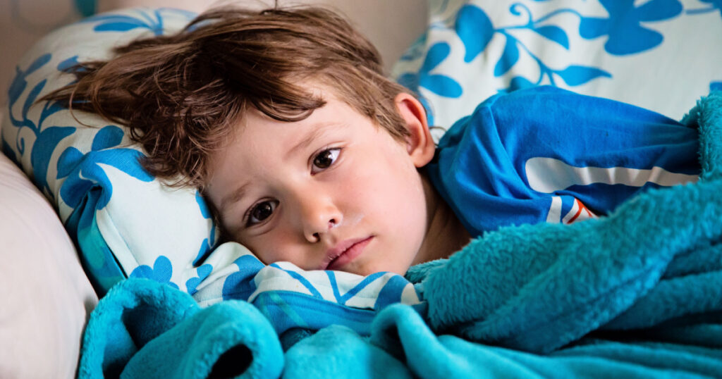 Sick child lying on couch at home having fever feeling ill. Getting well of flu. Kid with runny nose and sore throat