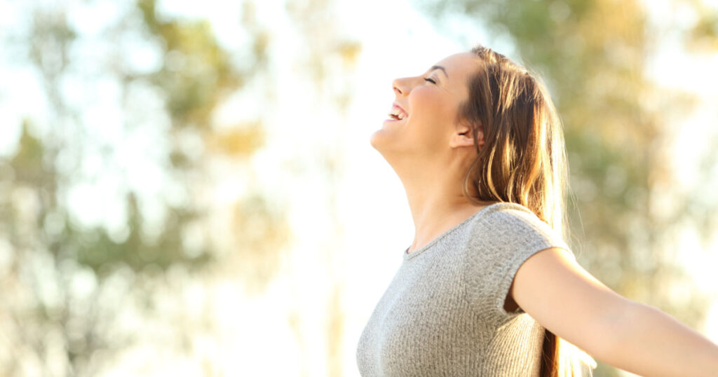 Side view portrait of a woman breathing fresh air outdoors in summer with trees and sky in the background