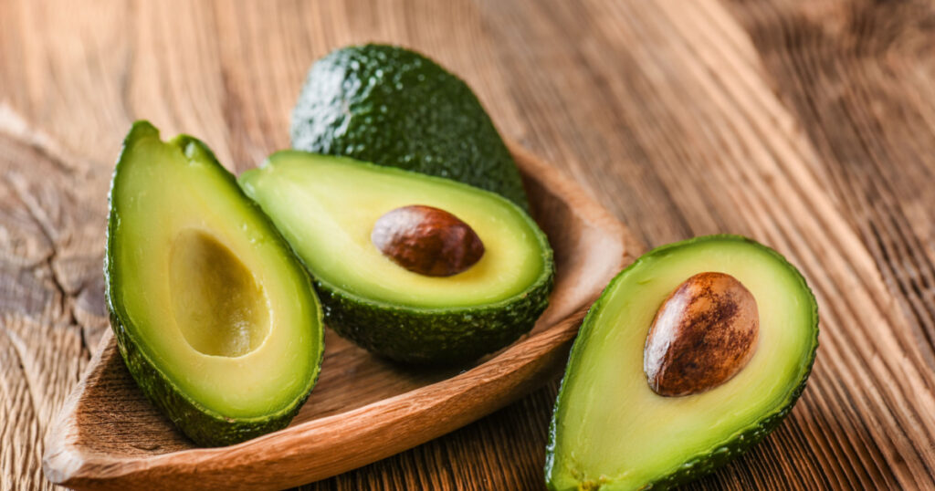 Avocado on old wooden table.Halfs on wooden bowl. Fruits healthy food concept.