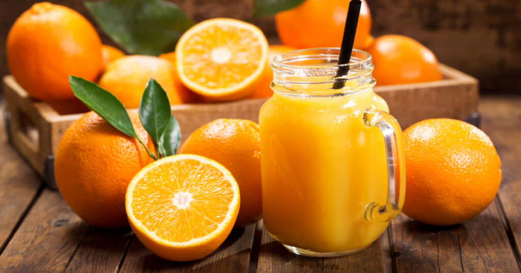 glass jar of fresh orange juice with fresh fruits on wooden table