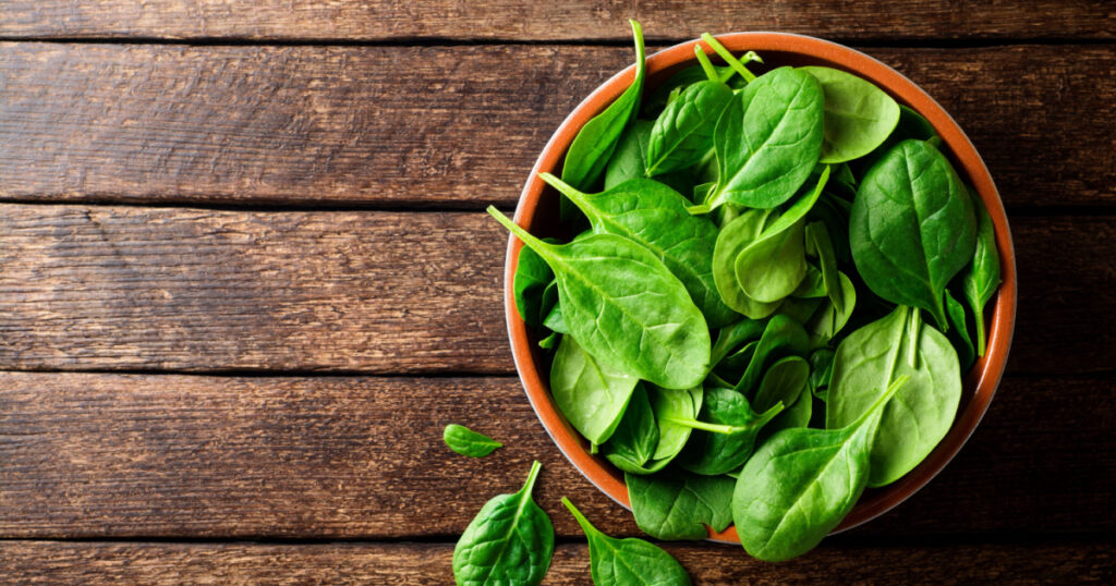 Fresh spinach leaves in bowl on rustic wooden table. Top view.