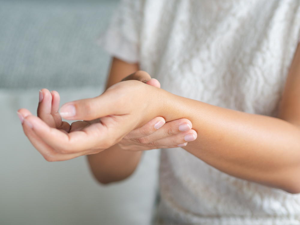 Closeup young woman sitting on sofa holds her wrist. hand injury, feeling pain. Health care and medical concept.