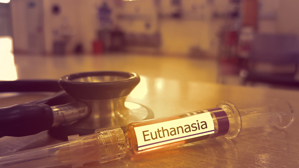 Syringe of medicine for mercy killing and stethoscope with blured hospital background. Euthanasia is practice of intentionally ending a life to relieve suffering from disease. End of life care concept