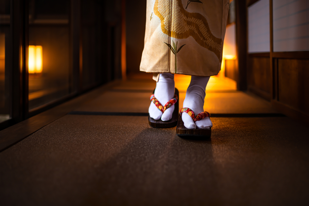 Traditional Japanese house ryokan closeup with tatami mat floor, shoji sliding paper doors and woman in kimono and geta shoes tabi socks walking in corridor hall room
