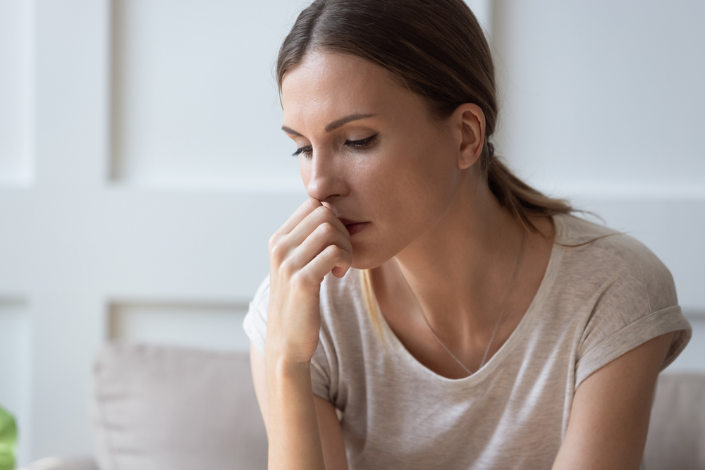 Close up of sad pensive millennial woman sit alone thinking about relationships personal problems, upset thoughtful young female lost in thoughts feel lonely depressed pondering or mourning at home
