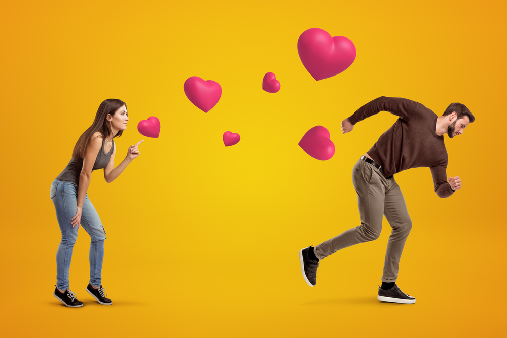 Side view of young girl following with her eyes young man who's running away being chased by cute valentine hearts that float in air on amber background. Young couple problems. St. Valentine's.