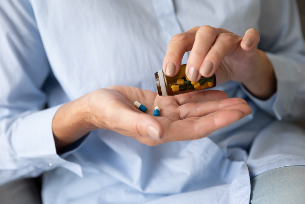 Close up old female hands holds glass bottle pours pills on palm taking daily dosage of medication, problem prevention, meds treat symptoms of Alzheimer, chronic senile diseases cure therapy concept
