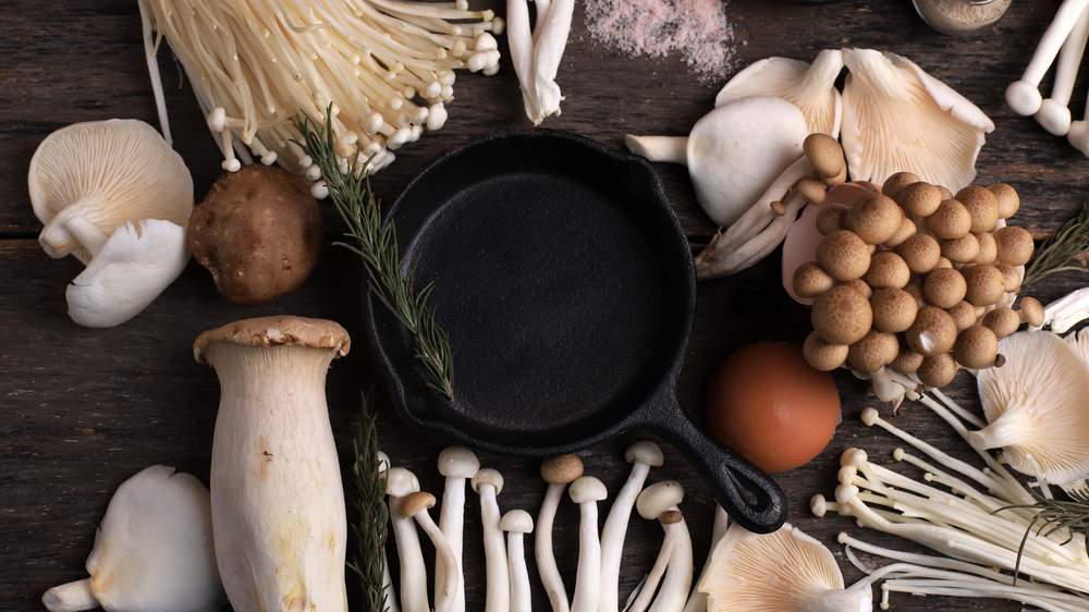 Cast Iron in the Center of Various Raw Mushroom Types - Portobello Mushrooms, Champignons, Shimeji, Enoki Mushrooms. Mushrooms Background, Rustic Mood Top View

