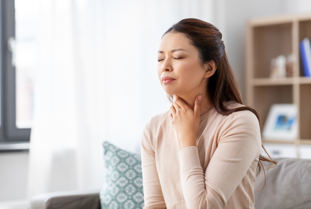 health, cold and people concept - sad sick young asian woman with sore throat at home