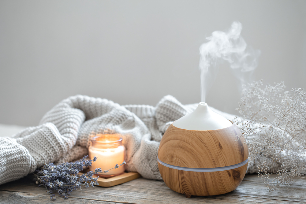 Aroma composition with a modern aroma oil diffuser on a wooden surface with a knitted element, candle and lavender.