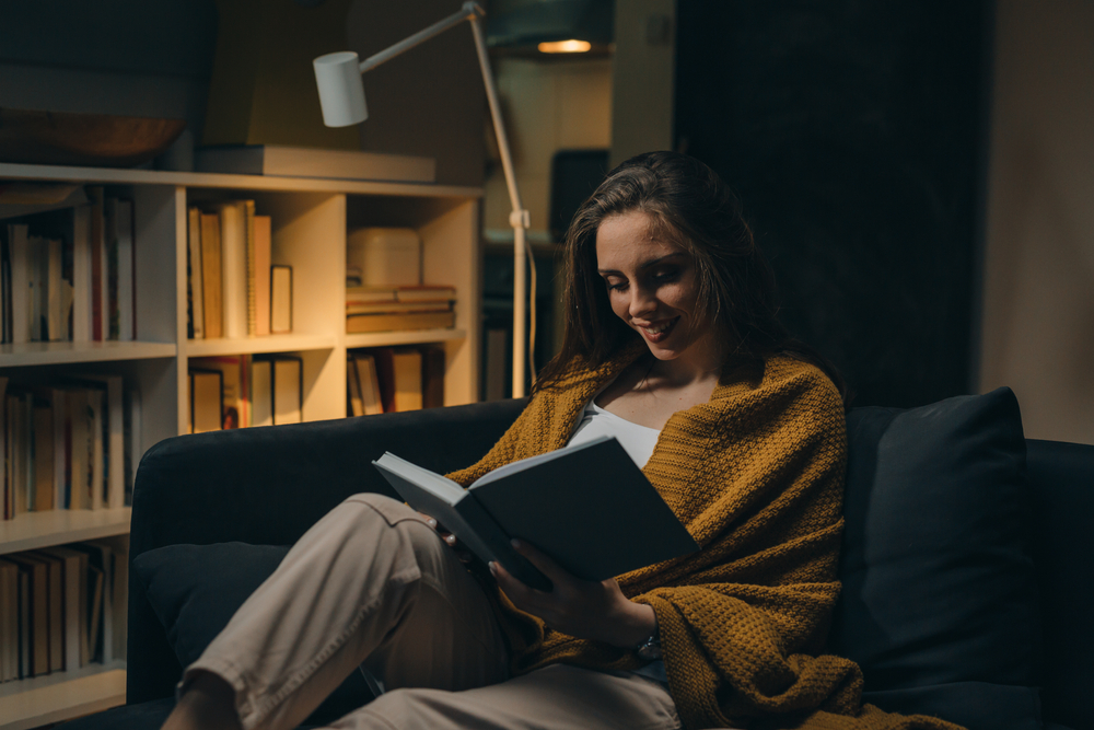 woman relaxing on sofa and reading book. evening moody ambience. she is enjoying time during weekend