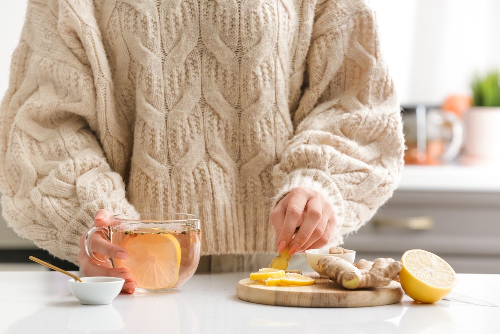 Woman making healthy tea with ginger and lemon in kitchen