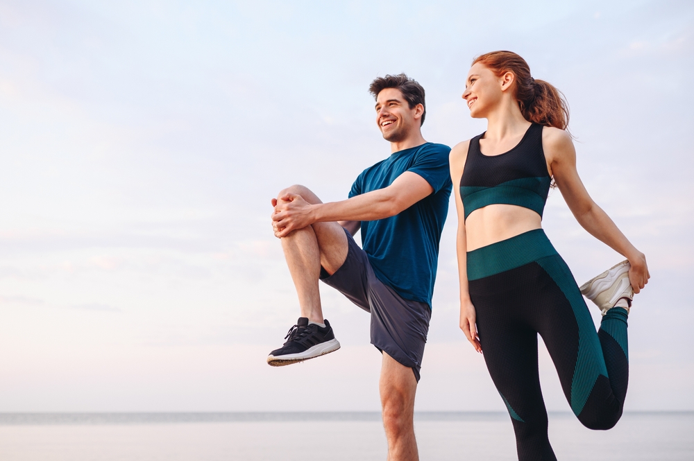 Lower couple young two friend strong sporty sportswoman sportsman woman man in sport clothes warm up training do stretch exercise on sand sea ocean beach outdoor jog on seaside in summer day morning
