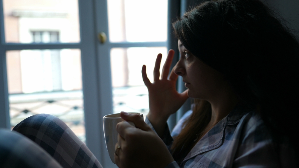 Woman removing sleep crust from eye in the morning wearing pajamas and holding cup of coffee
