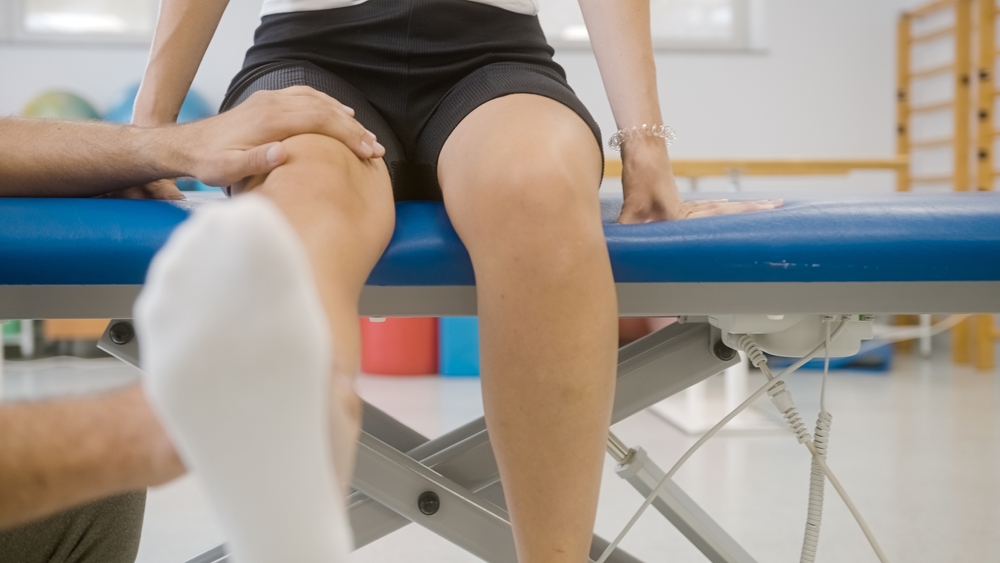Physiotherapist doing knee extension exercises with the female patient on the table
